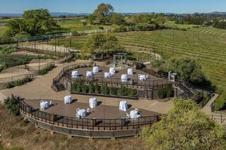 A scenic outdoor venue with circular patios, white tables, and lush vineyards in the background, perfect for events or gatherings.