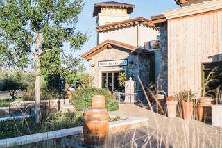 A scenic wine tasting facility featuring natural stone, wood elements, and decorative barrels, set amidst lush greenery and warm sunlight.