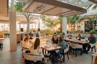 Guests enjoy an elegant dining experience surrounded by palm trees and a sunset glow, creating a warm and inviting atmosphere.