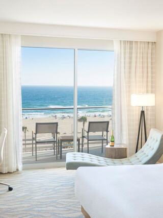 A bright, modern hotel room features a stunning ocean view, a comfortable lounge chair, and a bottle of champagne on display.