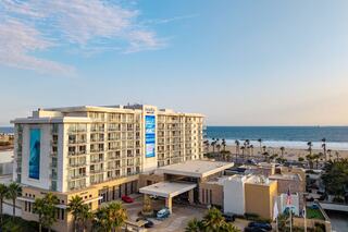 A modern beachfront hotel with balconies, surrounded by palm trees, overlooks the ocean, creating a picturesque coastal retreat.