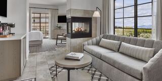 A stylish, modern hotel living space features a cozy sofa, a cozy fireplace, and large windows with scenic views, creating a warm and inviting atmosphere.